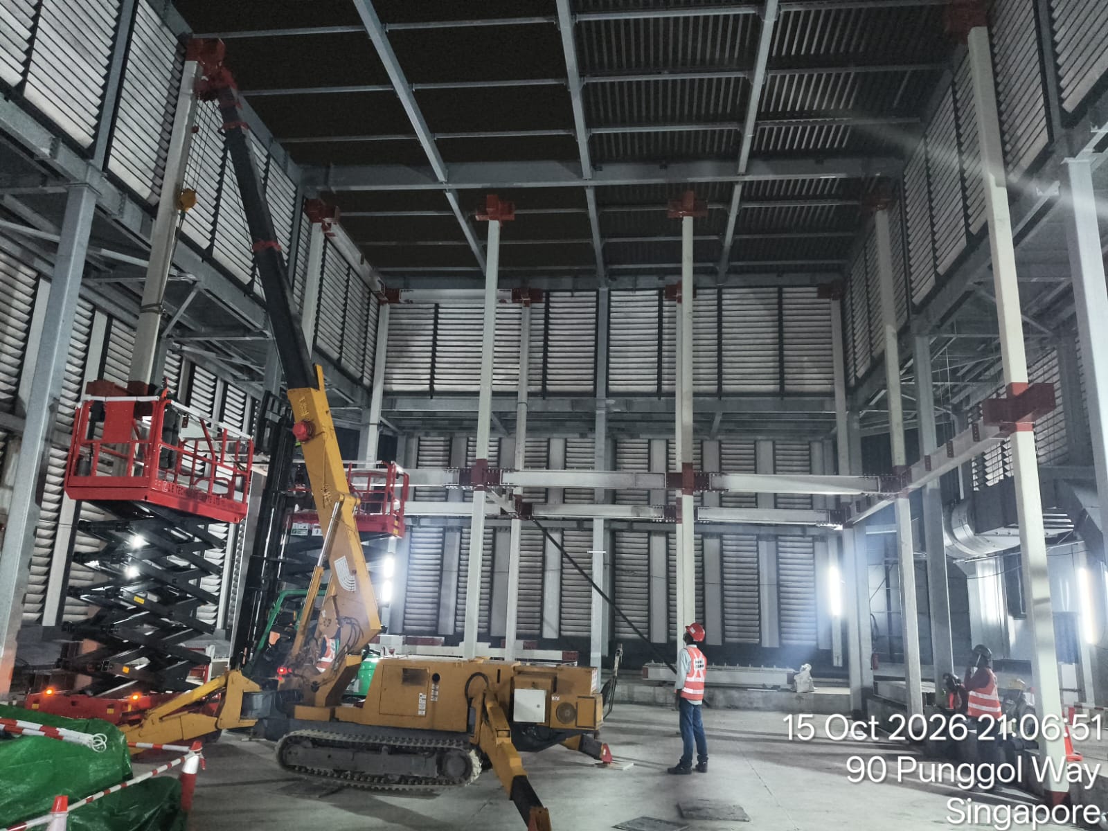 Spider crawler crane hoisting structural steel beams inside industrial building
